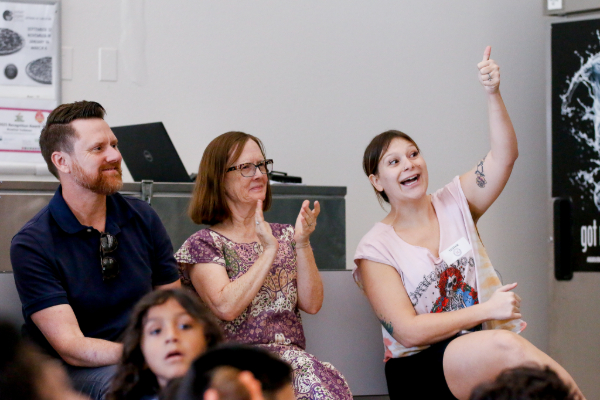 Parents in the audience clap and give thumbs up to support their students