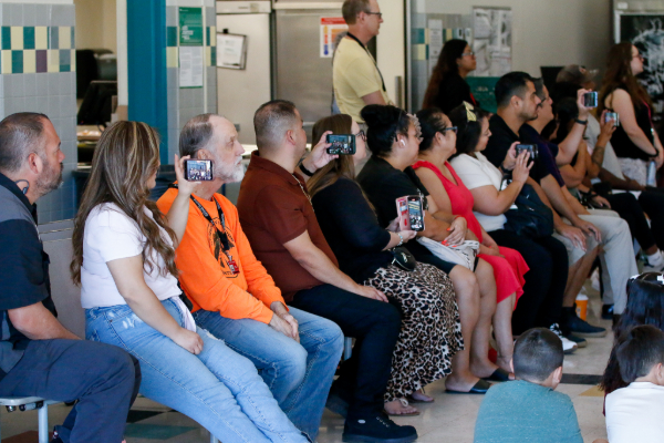 A row of parents taking photos and videos of their students performing