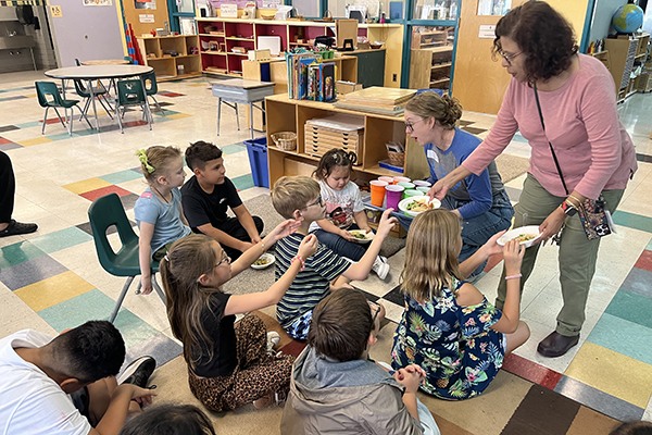 Students sitting on the floor eating bowls of food they helped make