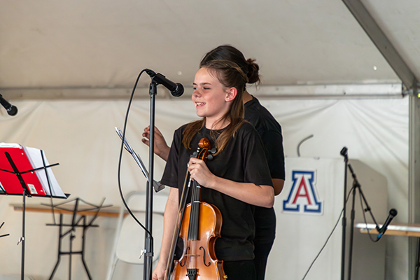 A girl smiles on stage holding her violin