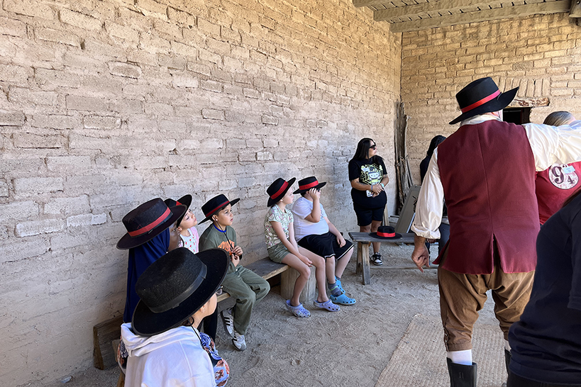 Students wearing black and red hats sit on benches