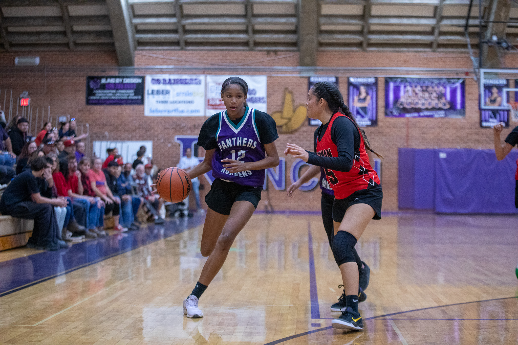 A girl in a red jersey blocks her opponent running the basketball down the court