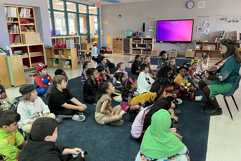 Students dressed in Halloween costumes sit on the floor