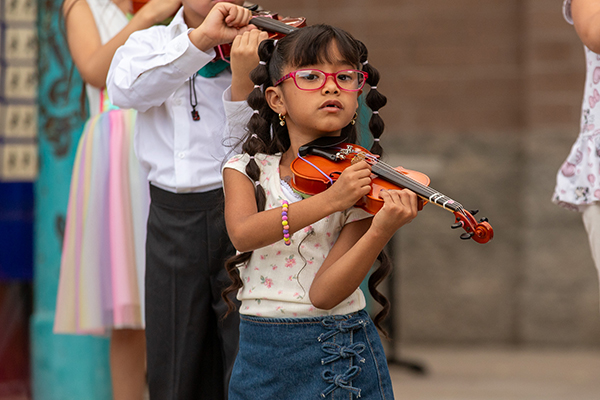 A little girl wearing glasses plays her violin