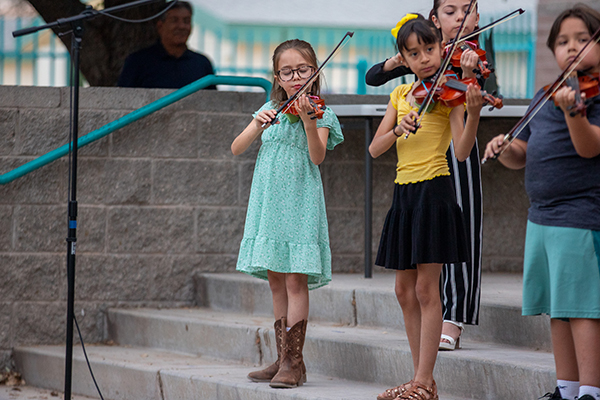 Young students stand on the steps outside playing their violins
