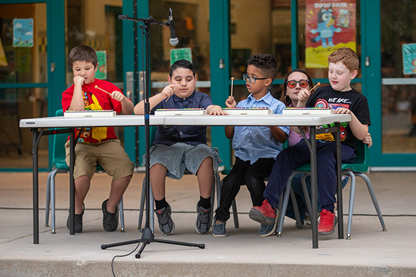 Four boys sit at a table playing xylophones