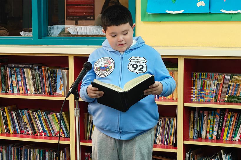A boy reads from a book into a microphone