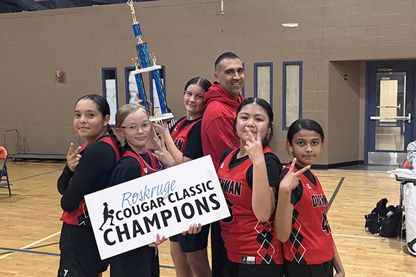 Girls basketball players pose with their trophy and their coach