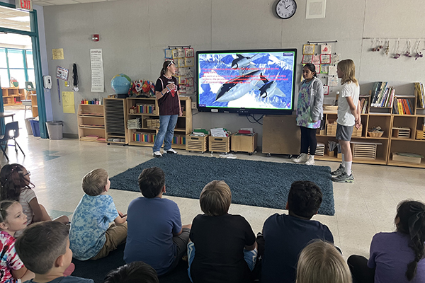 Students sit on the classroom floor watching a presentation about planes