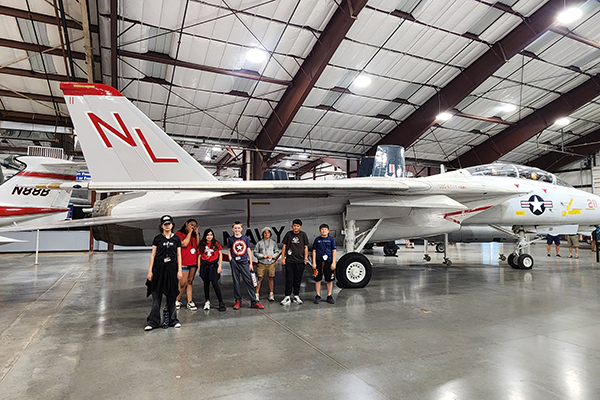 Students pose for a group photo by a plane in the hangar
