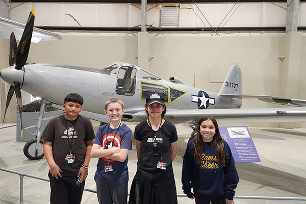Two boys and two girls pose for a photo by a plane in the hangar